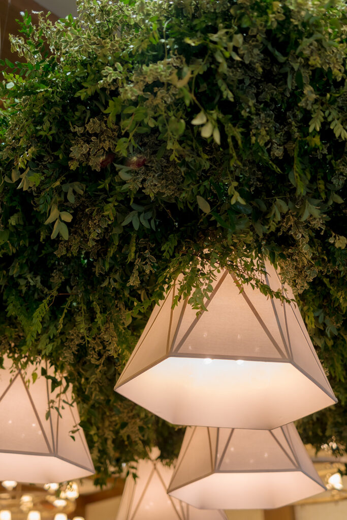 A lush, all-green dance floor installation is suspended in the air surrounding large light pendants. Featuring smilax, huckleberry branches and mini pitt greens, the dance floor has a moody yet lively focal point for guests to enjoy and dance under. Design by Rosemary and Finch Floral Design in Nashville, TN.