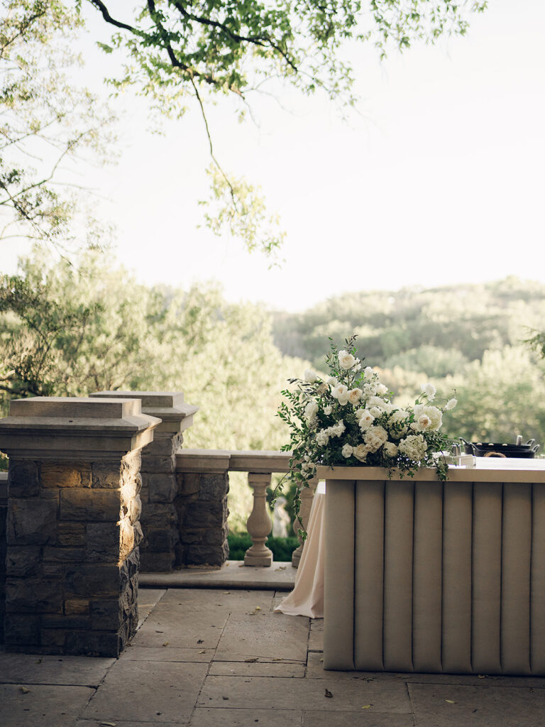 Simple and elegant floral arrangements for Cheekwood cocktail hour consisting of all-white bar arrangements and simple bud vases. Double tulips, hydrangeas, cloud and spray roses, delphinium, allium, riceflower, ranunculus, lisianthus, and white stock are used to create stunning floral moments scattered throughout the cocktail hour patio and bars. Design by Rosemary & Finch Floral Design in Nashville, TN.