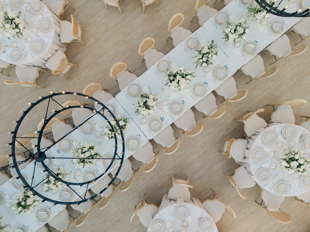 Romantic and stunning glass-tented wedding reception at Cheekwood botanical garden in Nashville, TN. Elegant garden-inspired centerpieces feature lush, all-white cloud roses, hydrangeas, lisianthus, dahlias, sweet peas, double tulips, delphinium, stock, allium, flowering champagne, and more with light greenery. Matching banquette meadows line either side of the glass tent creating a lush and timeless feel. Design by Rosemary & Finch Floral Design in Nashville, TN.