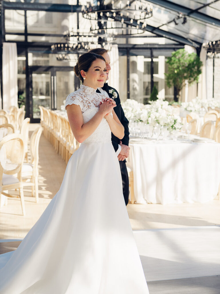 Romantic and stunning glass-tented wedding reception at Cheekwood botanical garden in Nashville, TN. Elegant garden-inspired centerpieces feature lush, all-white cloud roses, hydrangeas, lisianthus, dahlias, sweet peas, double tulips, delphinium, stock, allium, flowering champagne, and more with light greenery. Matching banquette meadows line either side of the glass tent creating a lush and timeless feel. Design by Rosemary & Finch Floral Design in Nashville, TN.